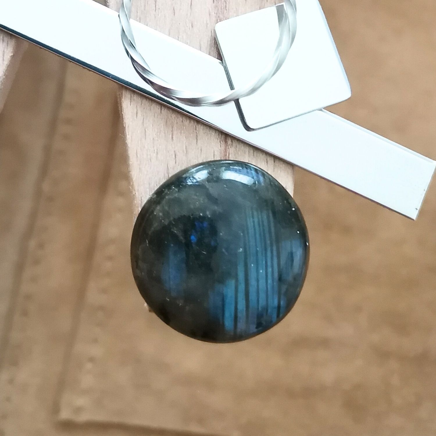 The round labradorite cabochon displayed on a jewellers bench peg with some sterling silver sheet and wire.