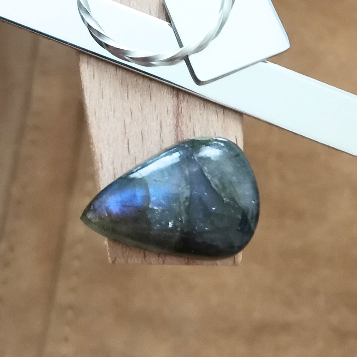 The teardrop labradorite cabochon displayed on a jewellers bench peg with some sterling silver sheet and wire.