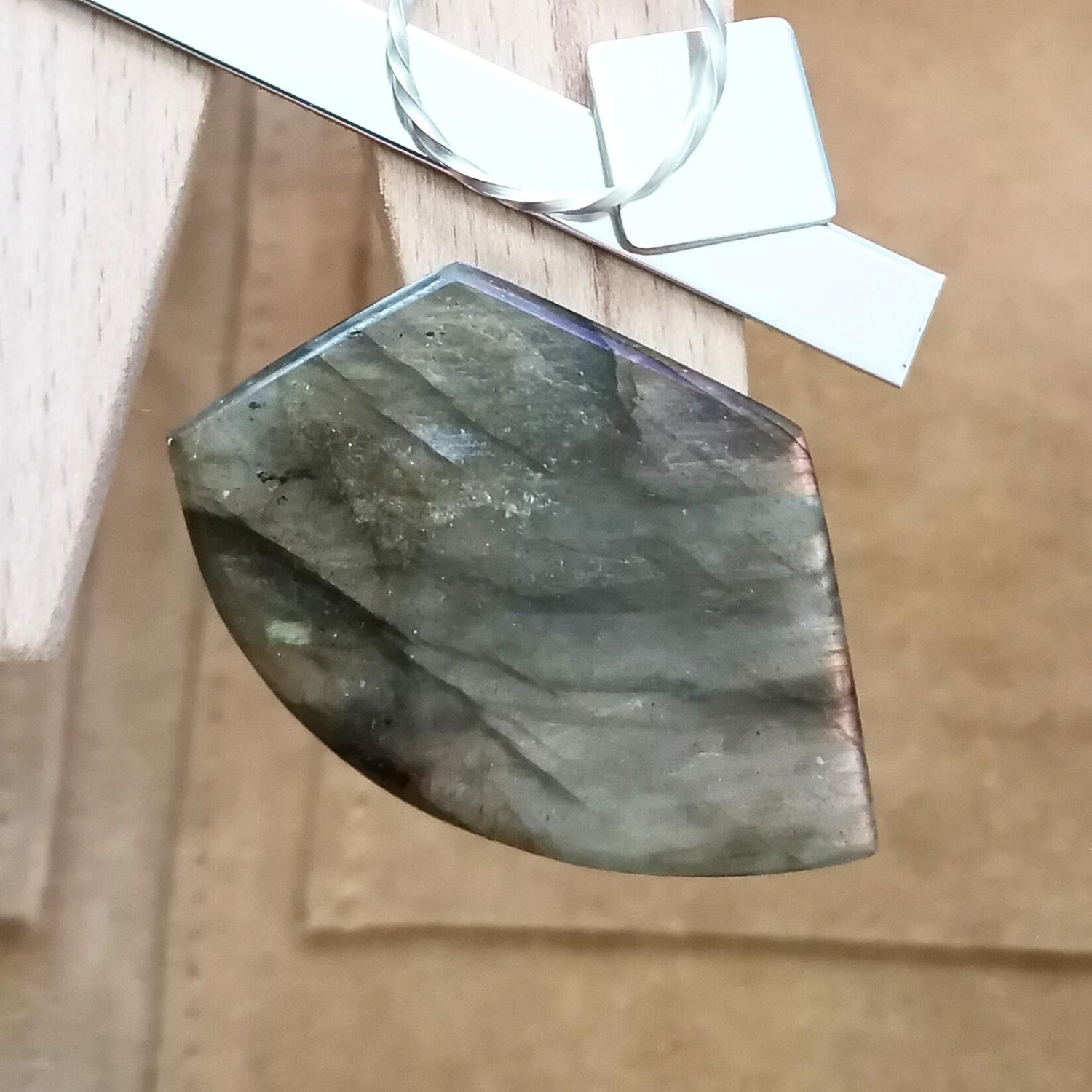 The large freeform labradorite cabochon displayed on a jewellers bench peg with some sterling silver sheet and wire.