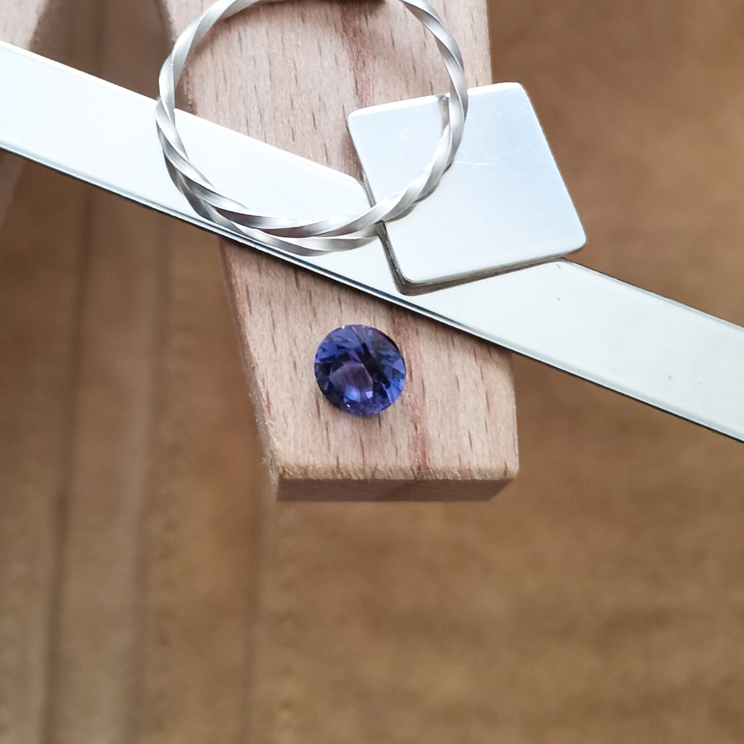 The round cut blue lab grown sapphire displayed on a jewellers bench peg with some sterling silver sheet and wire.