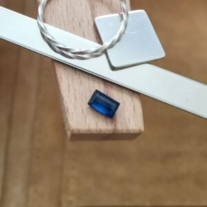 The rectangle cut blue lab grown sapphire displayed on a jewellers bench peg with some sterling silver sheet and wire.