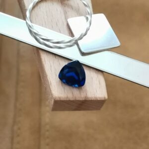 The cushioned triangle cut blue lab grown sapphire displayed on a jewellers bench peg with some sterling silver sheet and wire.