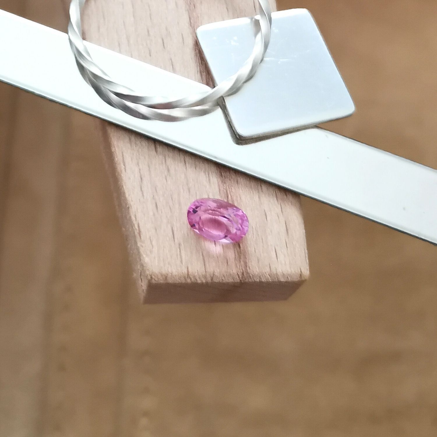 The oval cut pink lab grown sapphire displayed on a jewellers bench peg with some sterling silver sheet and wire.
