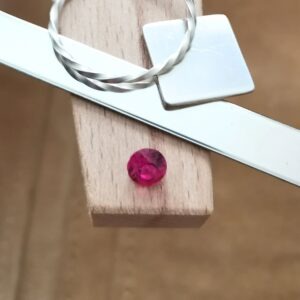The round dark pink lab grown sapphire displayed on a jewellers bench peg with some sterling silver sheet and wire.