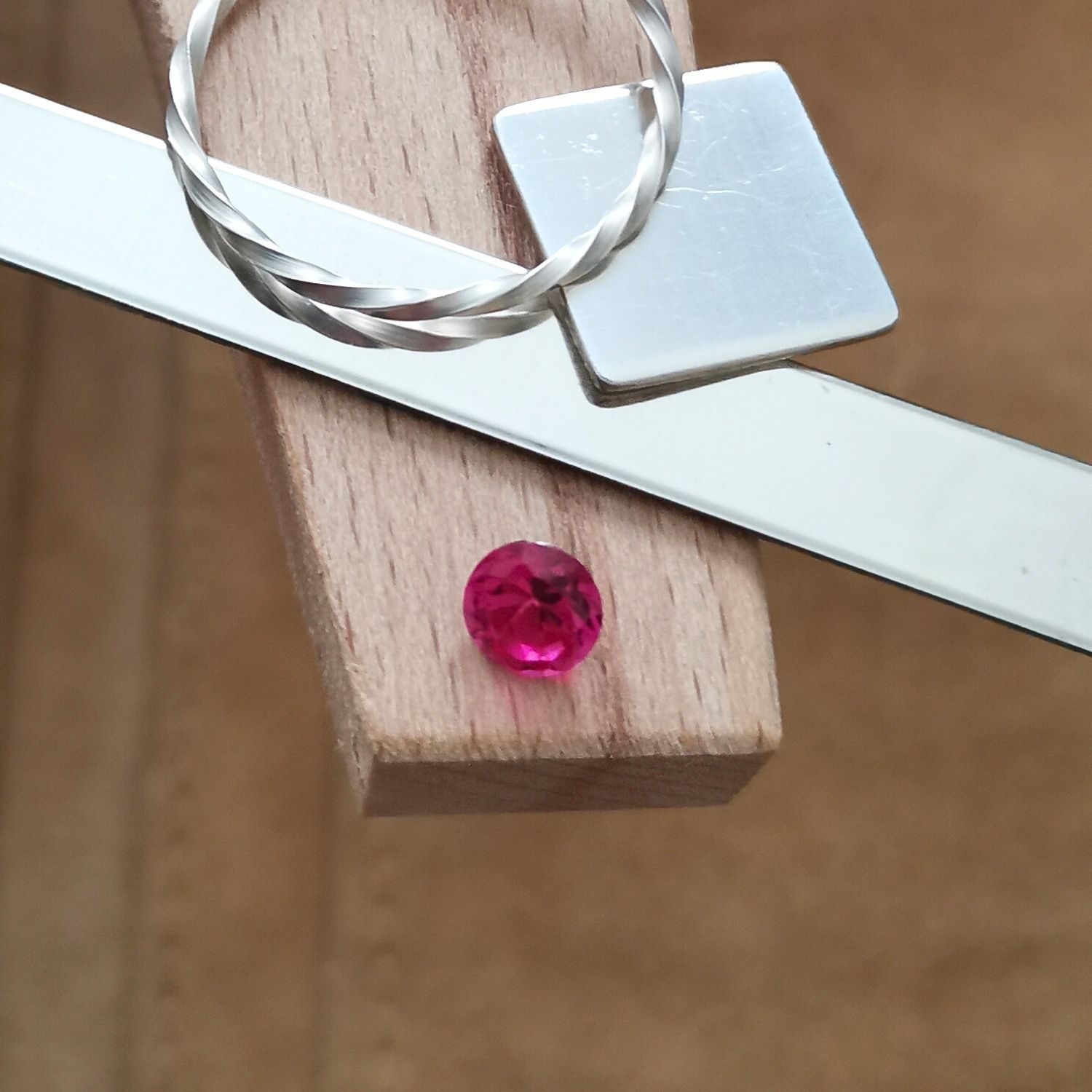 The round dark pink lab grown sapphire displayed on a jewellers bench peg with some sterling silver sheet and wire.