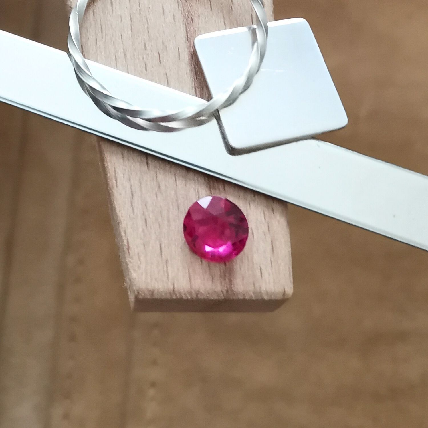The round dark pink lab grown sapphire displayed on a jewellers bench peg with some sterling silver sheet and wire.