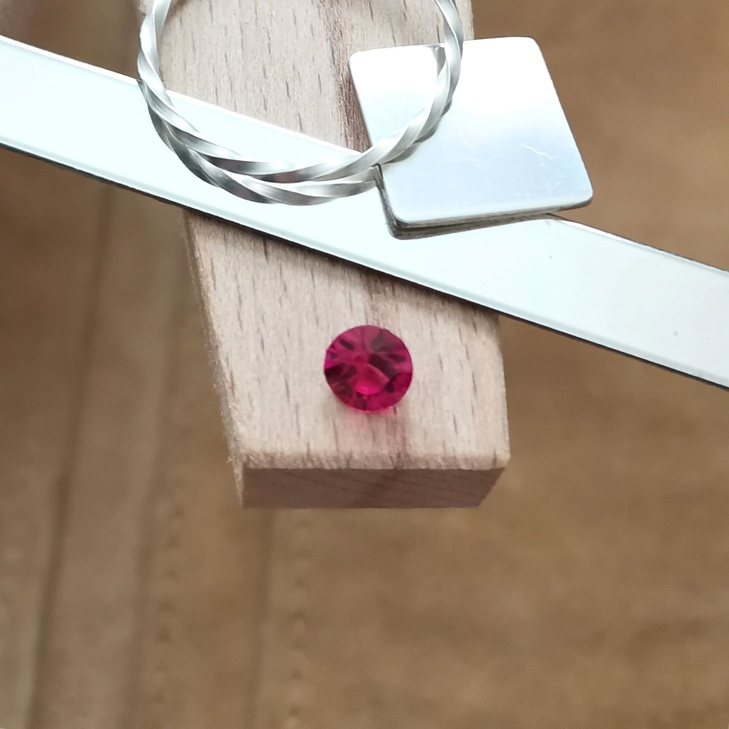 The round red lab grown ruby displayed on a jewellers bench peg with some sterling silver sheet and wire.