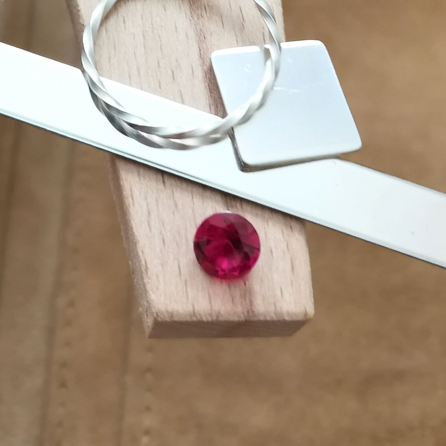 The round red lab grown ruby displayed on a jewellers bench peg with some sterling silver sheet and wire.