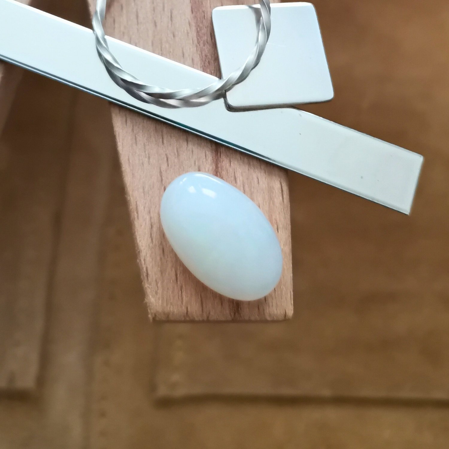 The white oval opal cabochon displayed on a jewellers bench peg with some sterling silver sheet and wire.