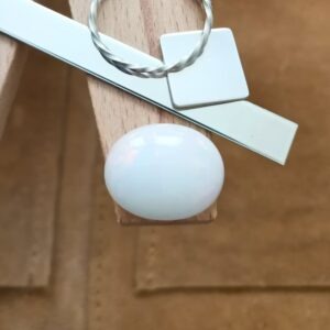 The white oval opal cabochon displayed on a jewellers bench peg with some sterling silver sheet and wire.