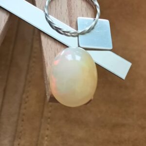 The orange oval opal cabochon displayed on a jewellers bench peg with some sterling silver sheet and wire.