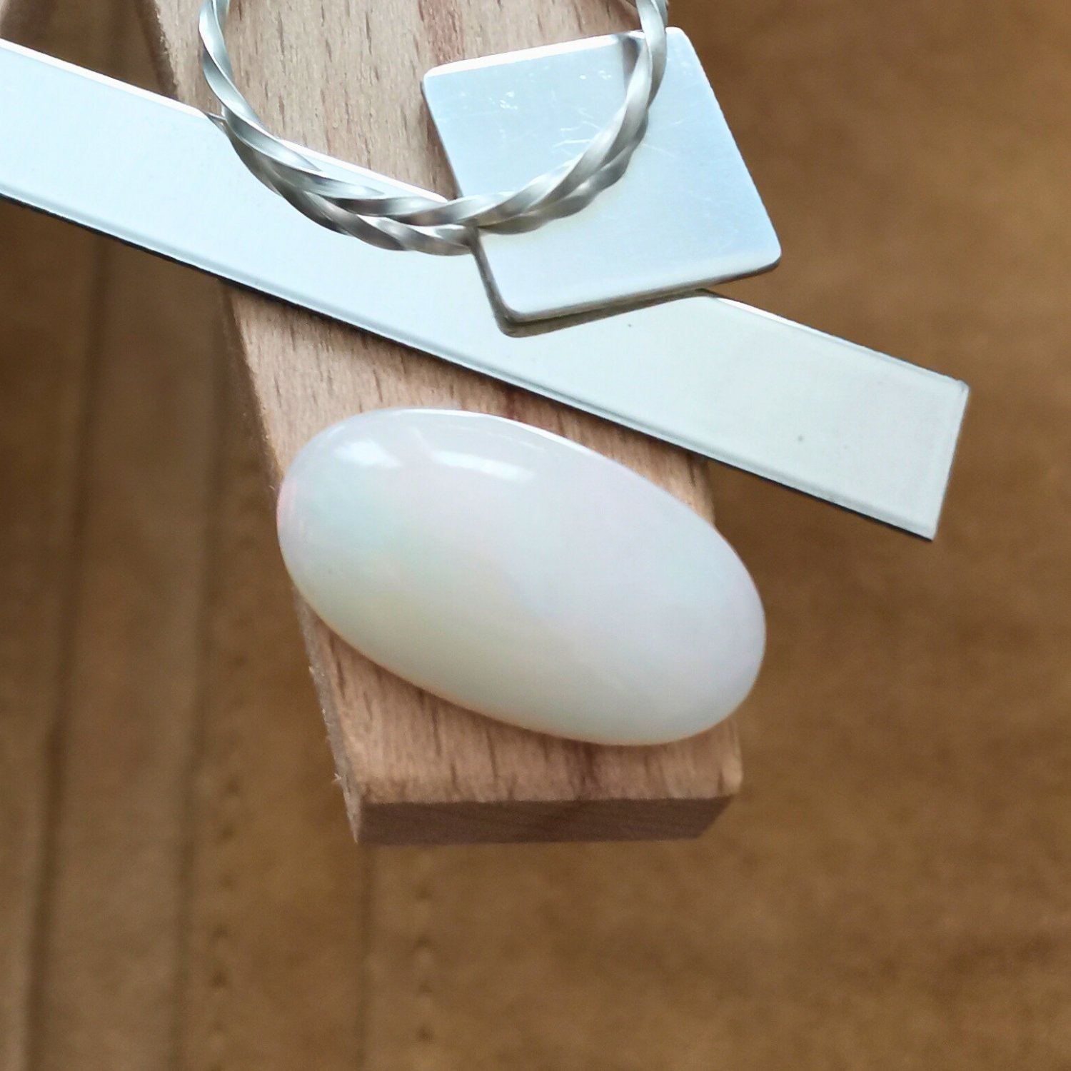 The white oval opal cabochon displayed on a jewellers bench peg with some sterling silver sheet and wire.