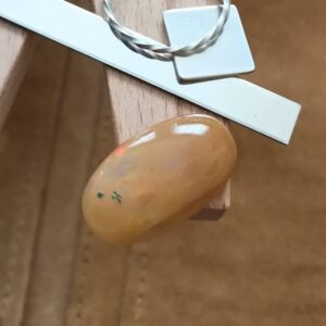 The orange oval opal cabochon displayed on a jewellers bench peg with some sterling silver sheet and wire.