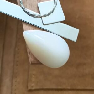 The white free form opal cabochon displayed on a jewellers bench peg with some sterling silver sheet and wire.