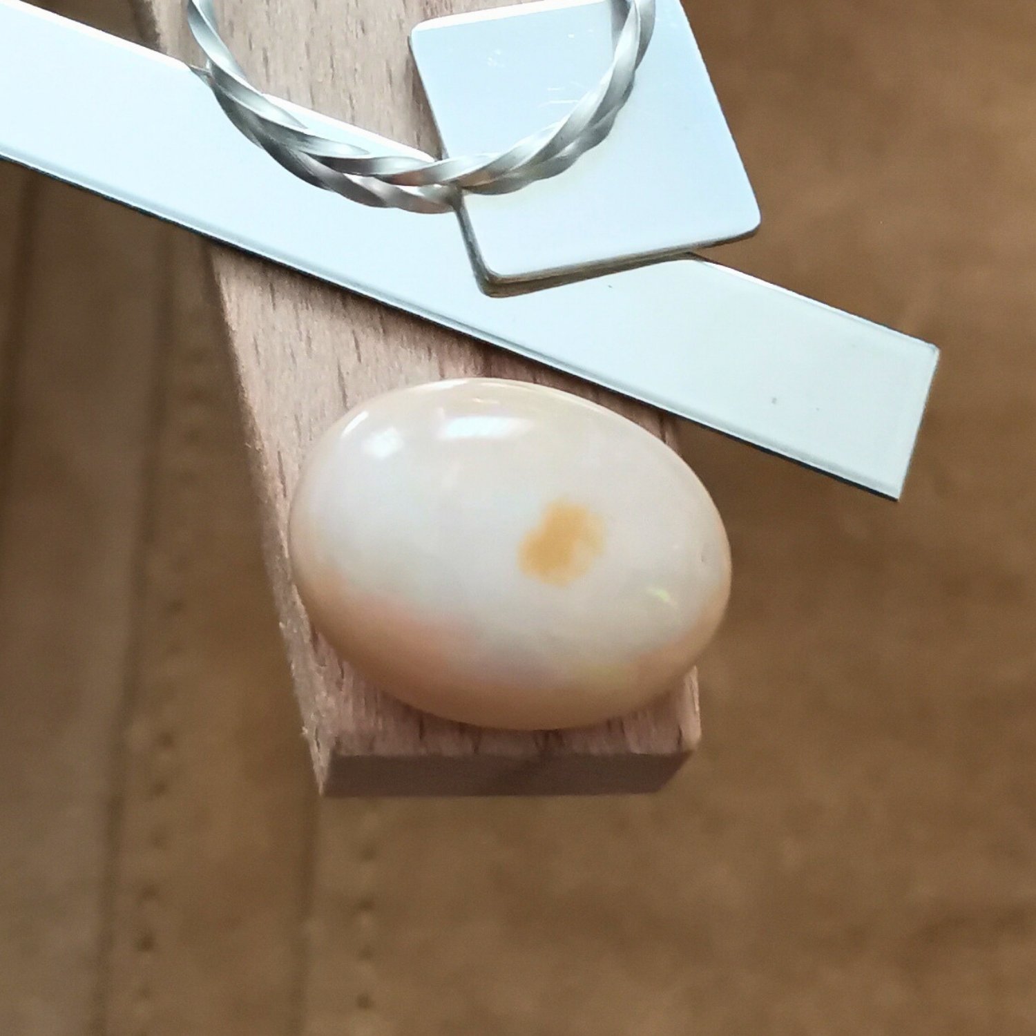 The orange oval opal cabochon displayed on a jewellers bench peg with some sterling silver sheet and wire.