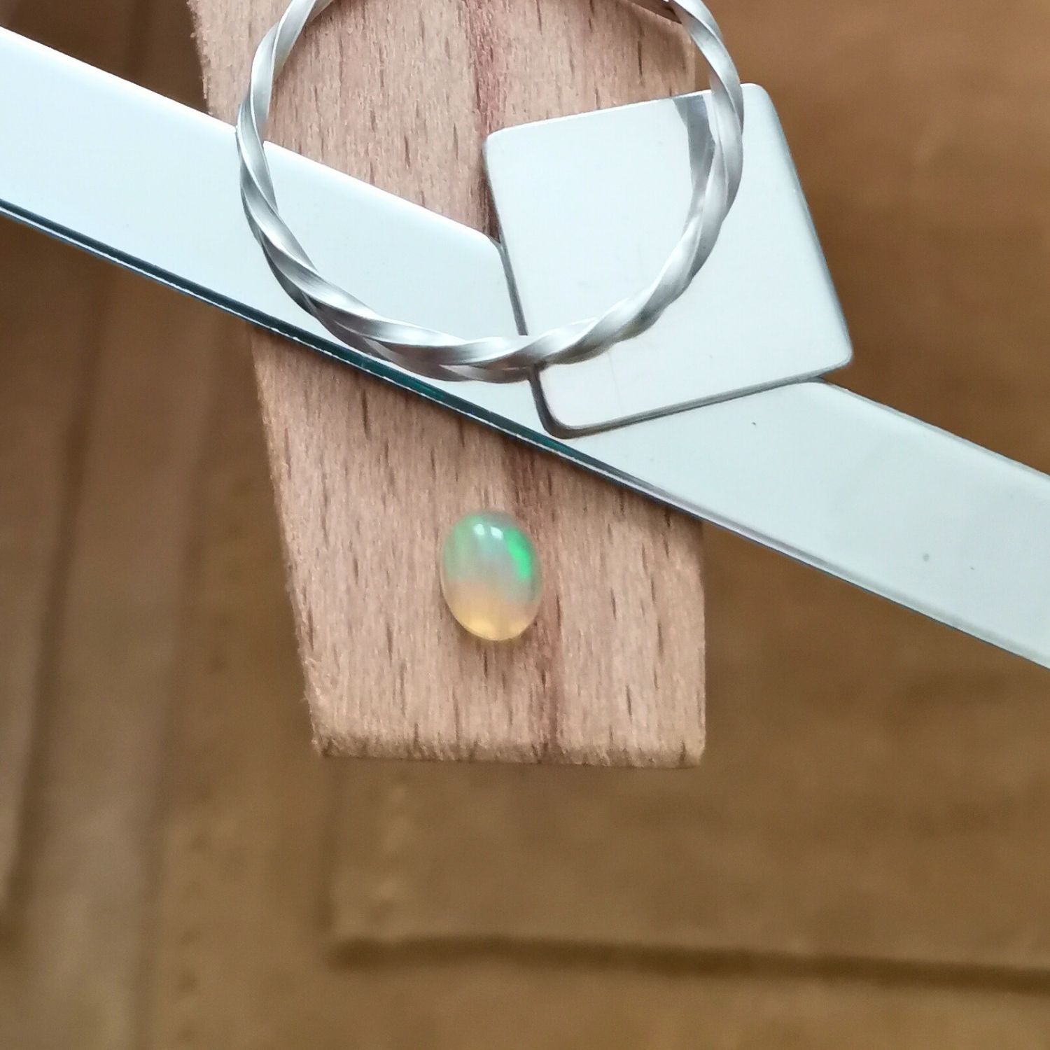 The small yellow oval opal cabochon displayed on a jewellers bench peg with some sterling silver sheet and wire.