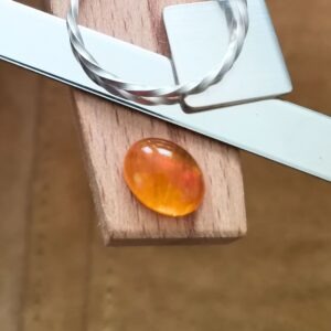 The oval fire opal cabochon displayed on a jewellers bench peg with some sterling silver sheet and wire.