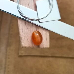 The orange oval cat's eye opal cabochon displayed on a jewellers bench peg with some sterling silver sheet and wire.