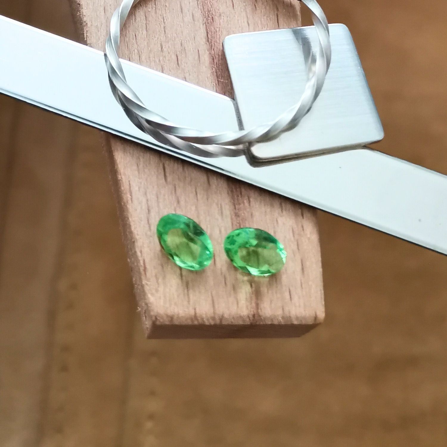 The pair of faceted green uranium glass ovals displayed on a jewellers bench peg with some sterling silver sheet and wire.