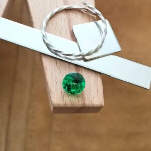 The round facet cut green YAG gemstone displayed on a jewellers bench peg with some sterling silver sheet and wire.