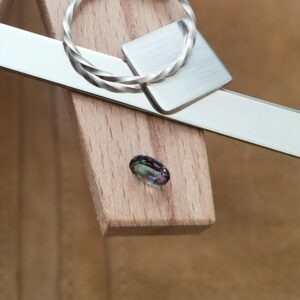 The mystic topaz oval displayed on a jewellers bench peg with some sterling silver sheet and wire.