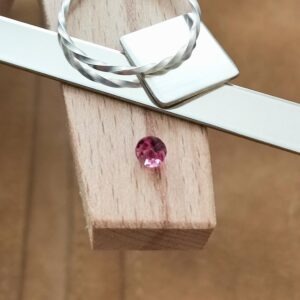 The dark pink topaz round displayed on a jewellers bench peg with some sterling silver sheet and wire.