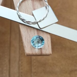 The faceted round blue topaz displayed on a jewellers bench peg with some sterling silver sheet and wire.