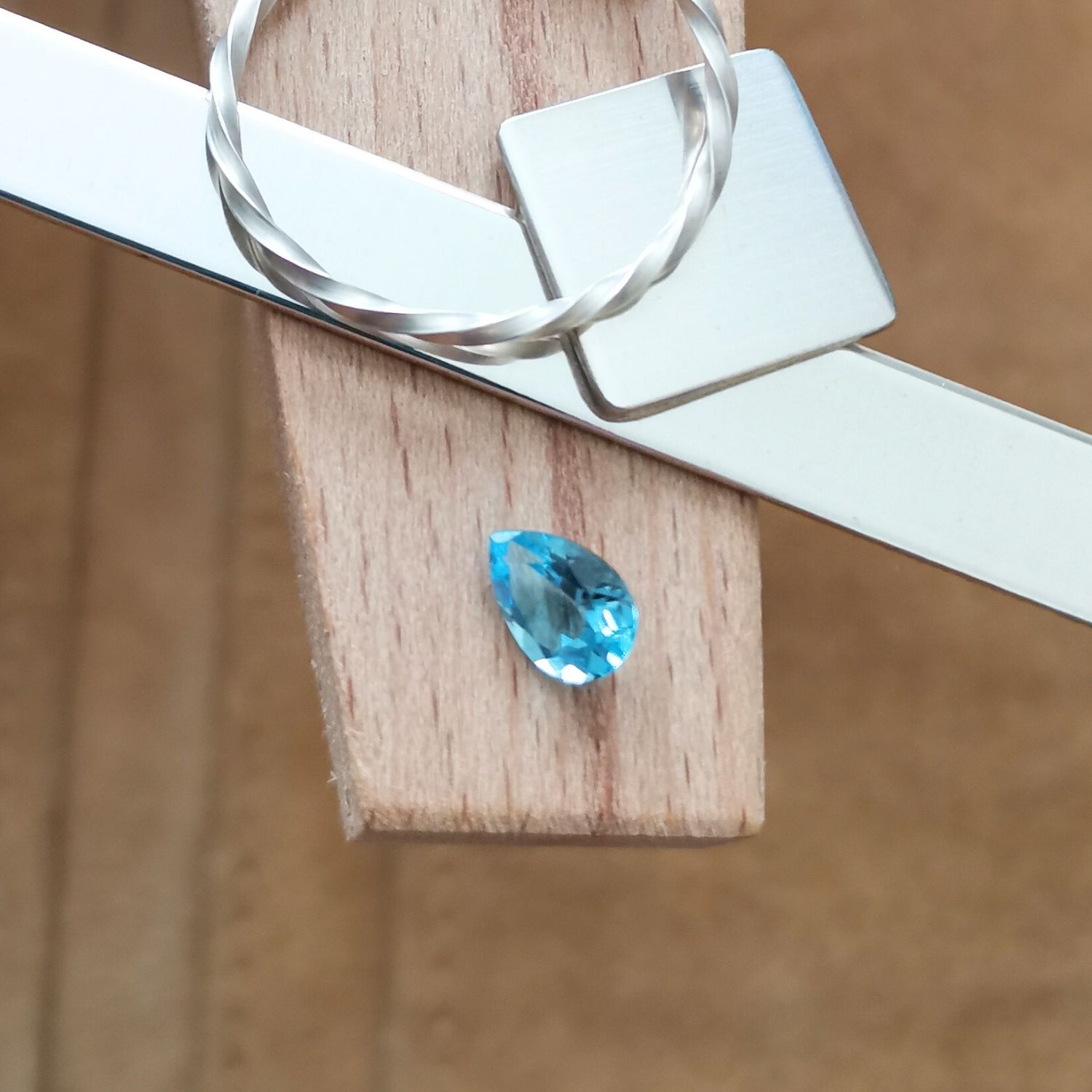 The blue topaz teardrop displayed on a jewellers bench peg with some sterling silver sheet and wire.