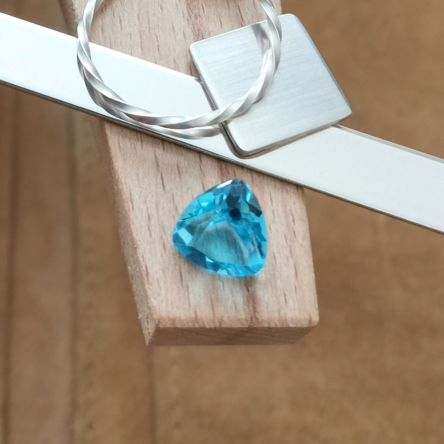 The blue topaz triangle displayed on a jewellers bench peg with some sterling silver sheet and wire.
