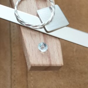 The colourless round cut goshenite displayed on a jewellers bench peg with some sterling silver sheet and wire.