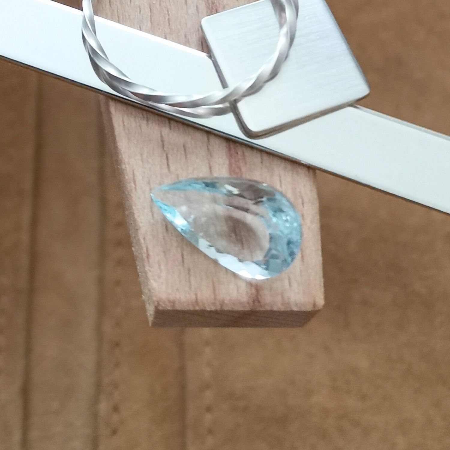 The blue aquamarine teardrop displayed on a jewellers bench peg with some sterling silver sheet and wire.
