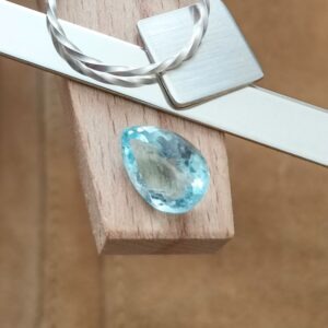 The pale blue aquamarine teardrop displayed on a jewellers bench peg with some sterling silver sheet and wire.