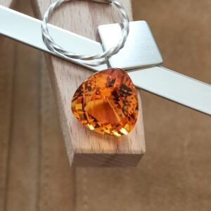The fancy facet cut orange citrine triangle displayed on a jewellers bench peg with some sterling silver sheet and wire.