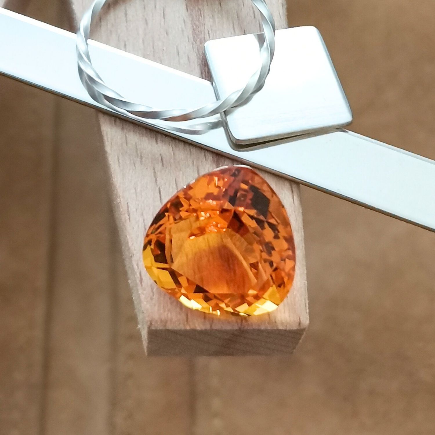 The large orange citrine triangle displayed on a jewellers bench peg with some sterling silver sheet and wire.