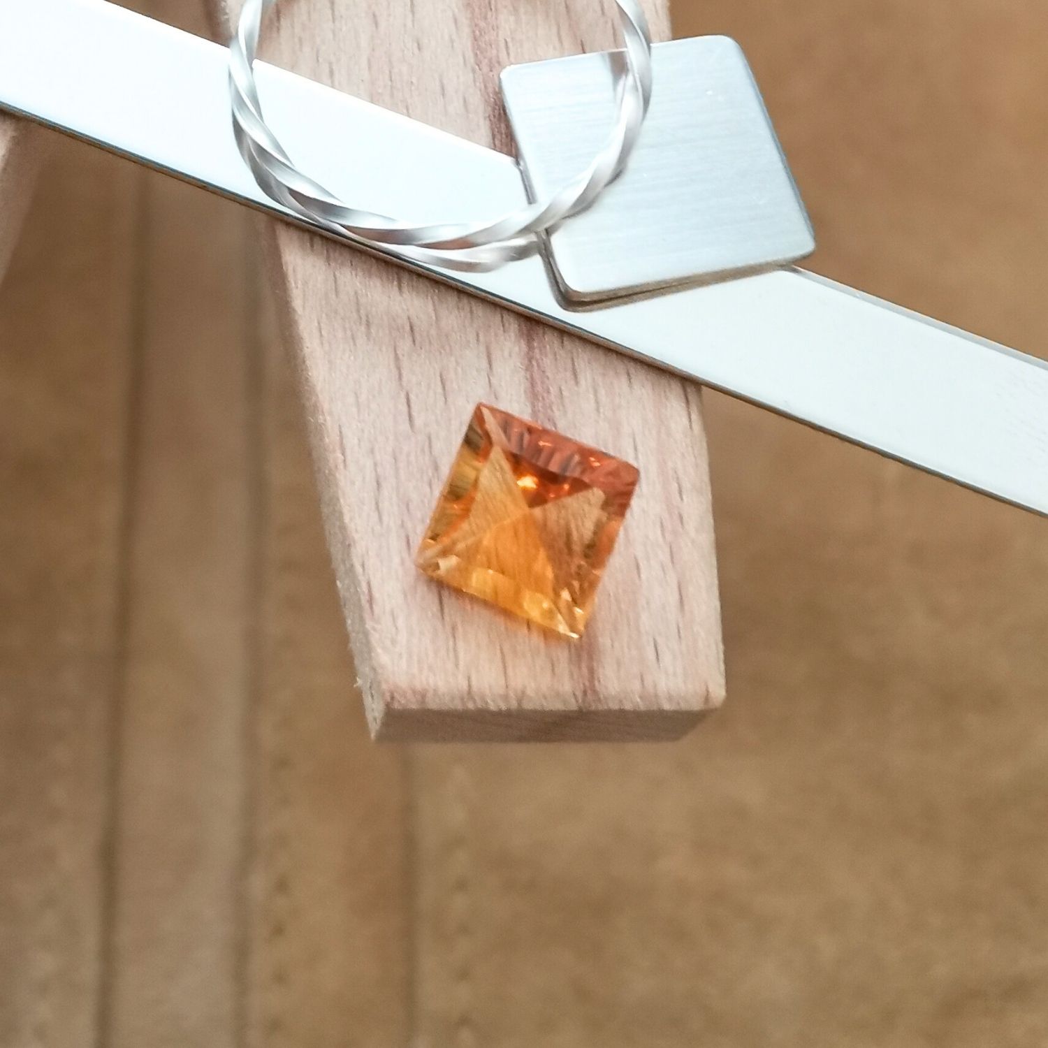 The faceted square cut orange citrine displayed on a jewellers bench peg with some sterling silver sheet and wire.