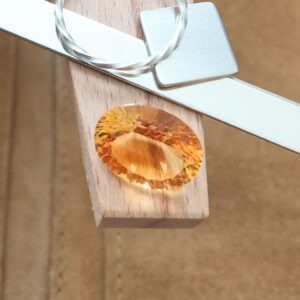 The orange citrine oval displayed on a jewellers bench peg with some sterling silver sheet and wire.