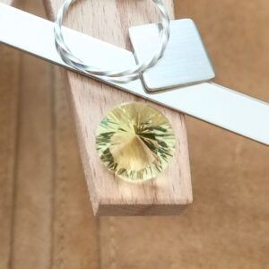 The faceted round cut yellow citrine displayed on a jewellers bench peg with some sterling silver sheet and wire.