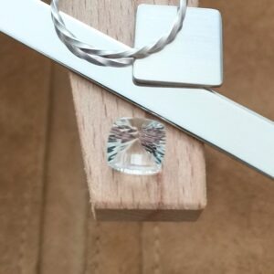 The faceted square clear quartz displayed on a jewellers bench peg with some sterling silver sheet and wire.