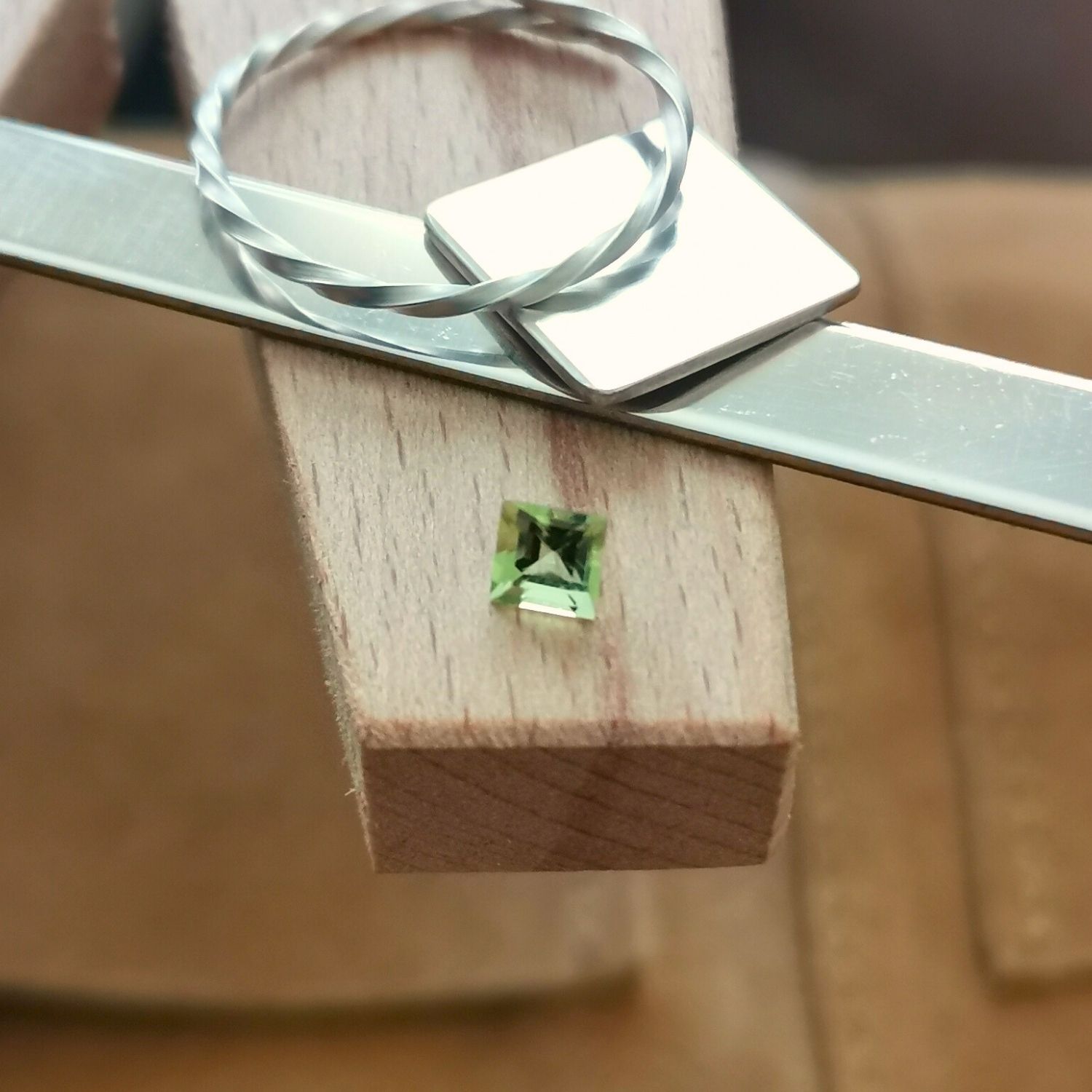 The small square cut peridot displayed on a jewellers bench peg with some sterling silver sheet and wire.