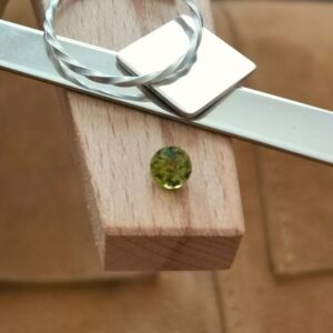 The olive green peridot round displayed on a jewellers bench peg with some sterling silver sheet and wire.