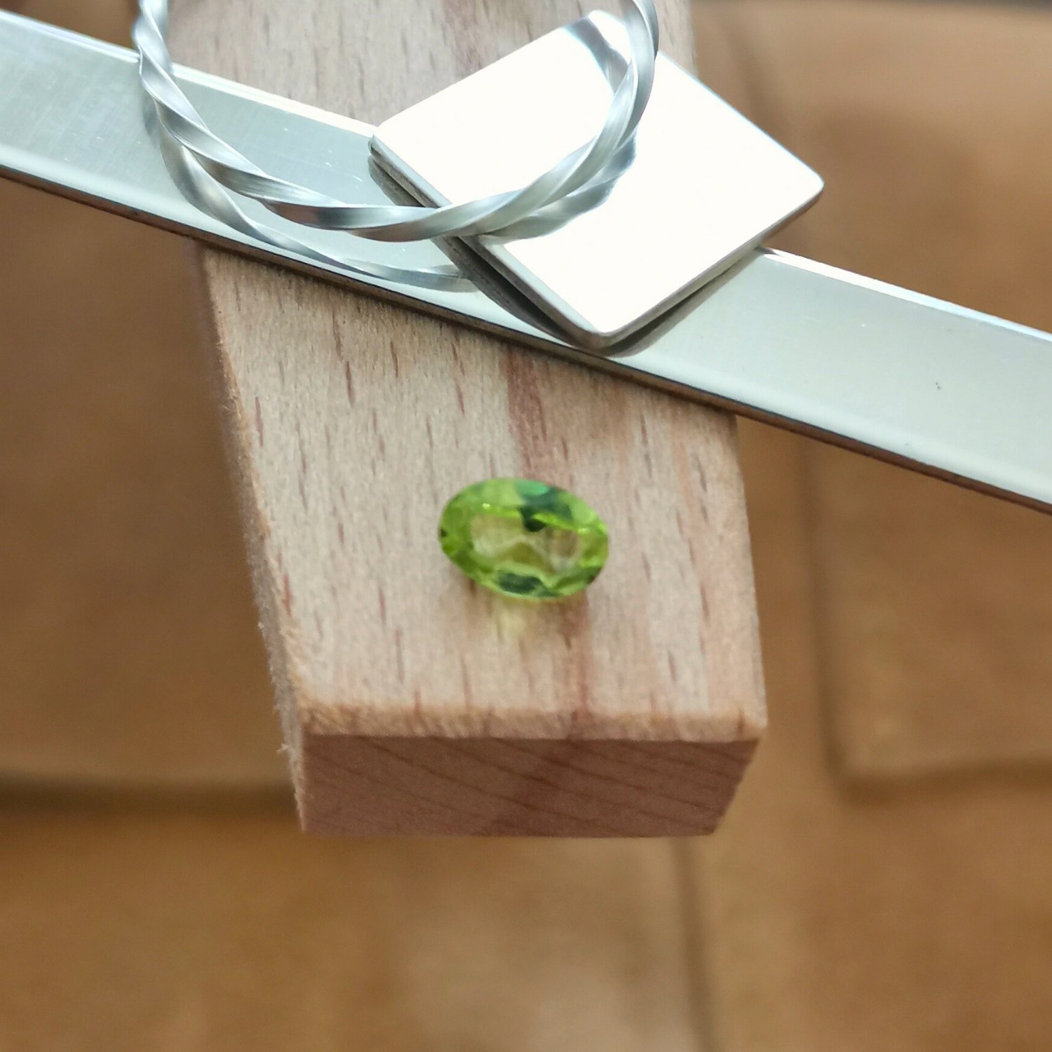 The oval shaped facet cut peridot displayed on a jewellers bench peg with some sterling silver sheet and wire.