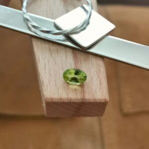 The green peridot oval displayed on a jewellers bench peg with some sterling silver sheet and wire.