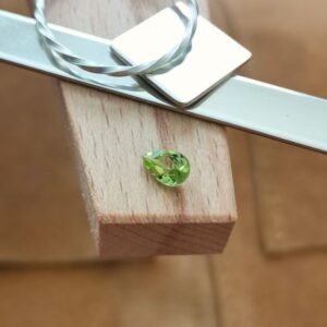 The bright green faceted teardrop peridot displayed on a jewellers bench peg with some sterling silver sheet and wire.