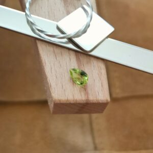 The small peridot teardrop displayed on a jewellers bench peg with some sterling silver sheet and wire.
