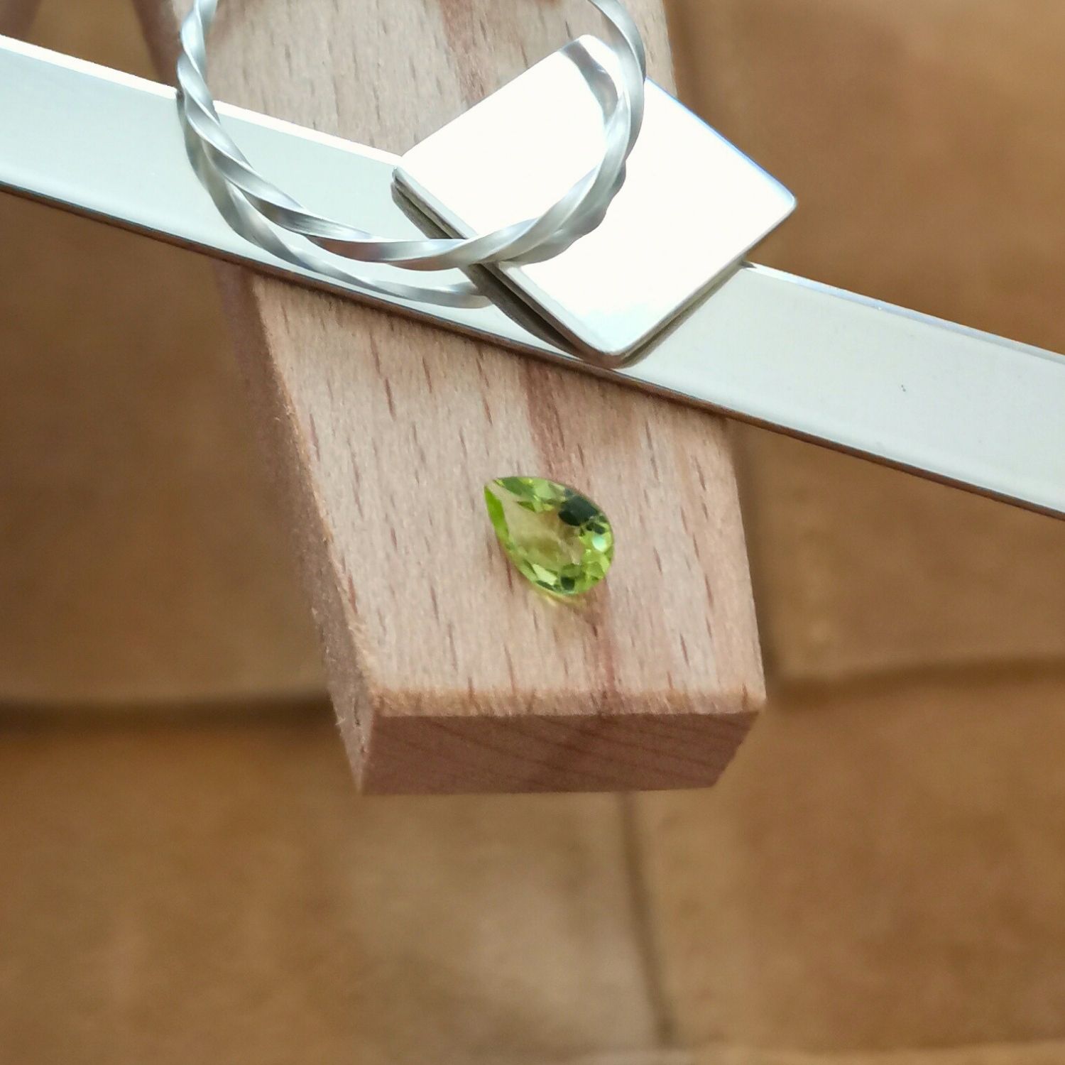 The small peridot teardrop displayed on a jewellers bench peg with some sterling silver sheet and wire.