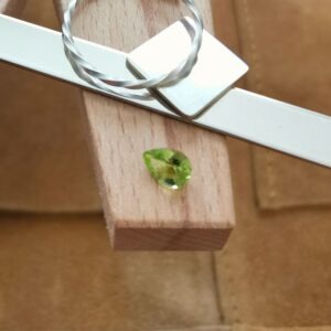 The fresh green peridot teardrop displayed on a jewellers bench peg with some sterling silver sheet and wire.