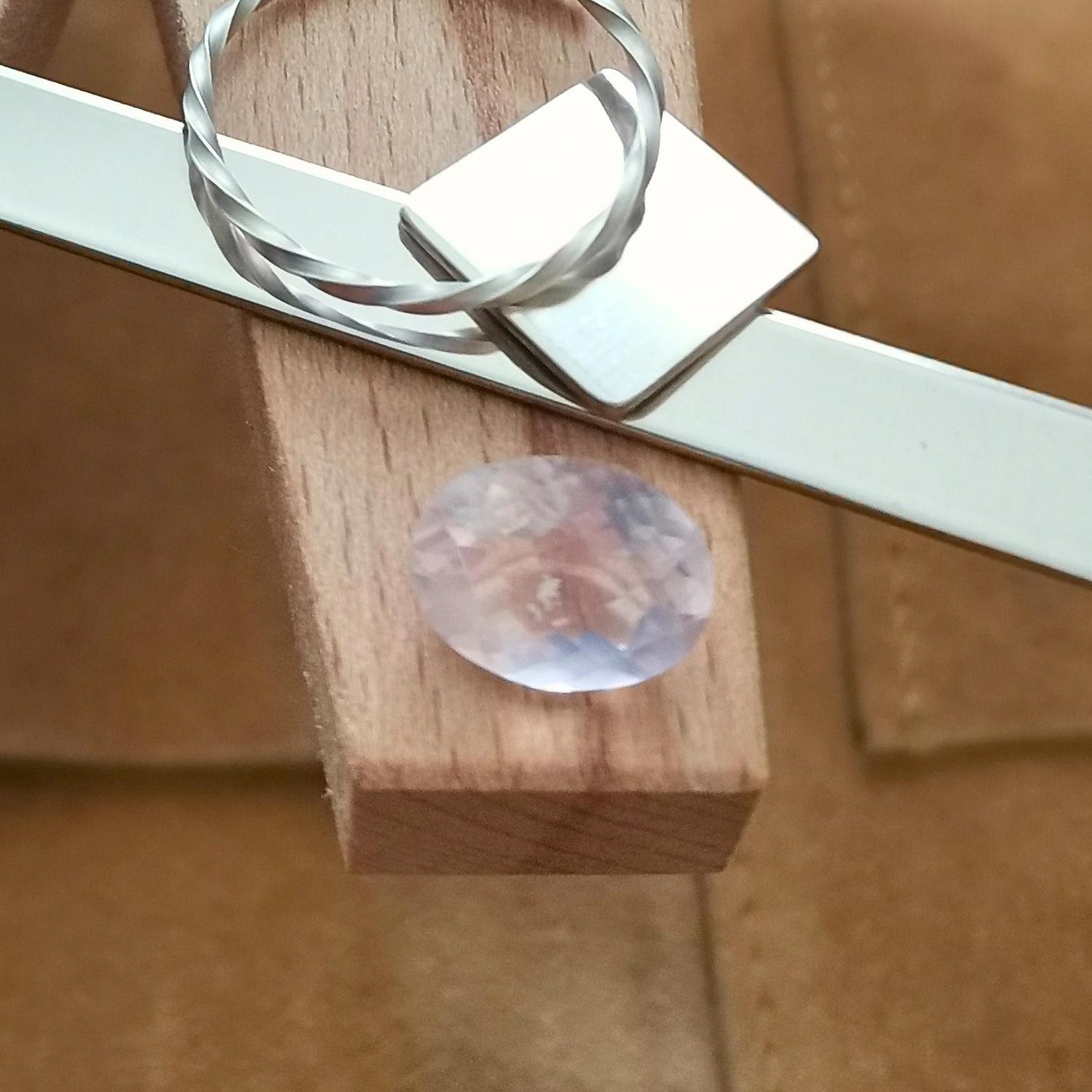 The oval cut rose quartz displayed on a jewellers bench peg with some sterling silver sheet and wire.