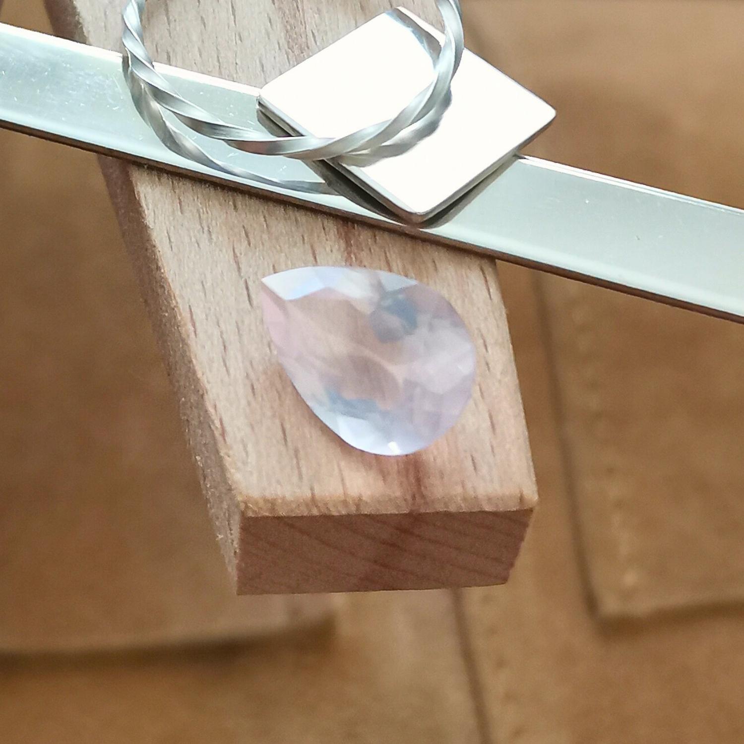 The faceted rose quartz teardrop displayed on a jewellers bench peg with some sterling silver sheet and wire.