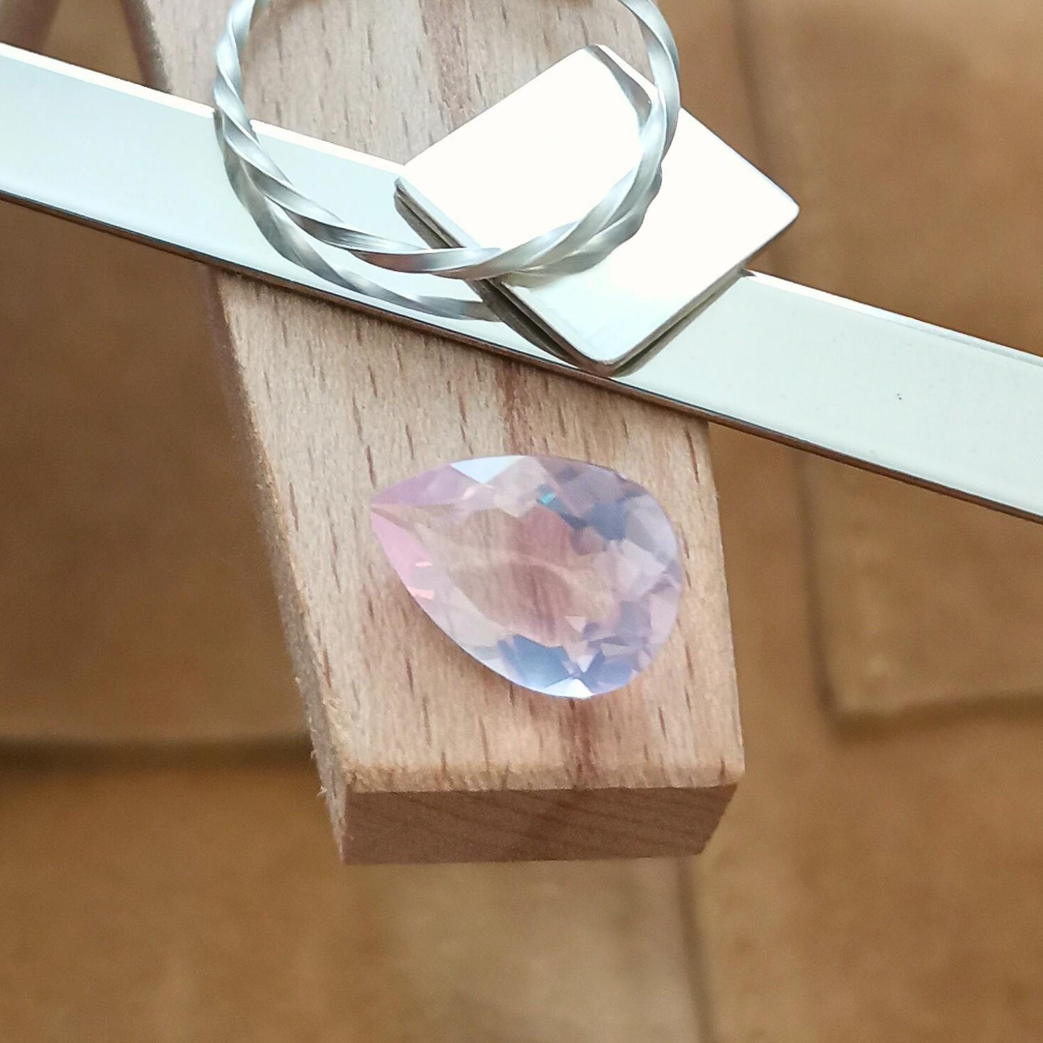 The pale pink rose quartz teardrop displayed on a jewellers bench peg with some sterling silver sheet and wire.