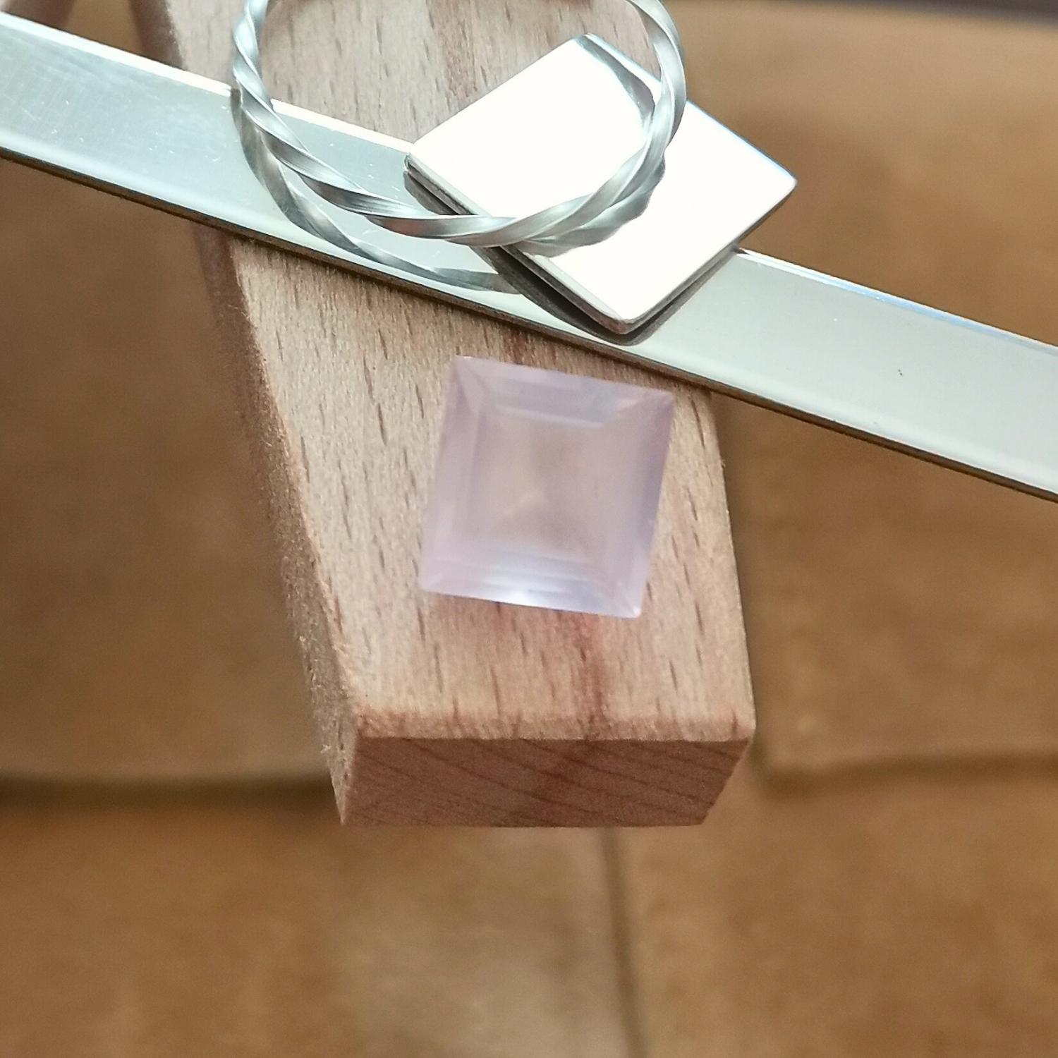 The faceted rose quartz square displayed on a jewellers bench peg with some sterling silver sheet and wire.